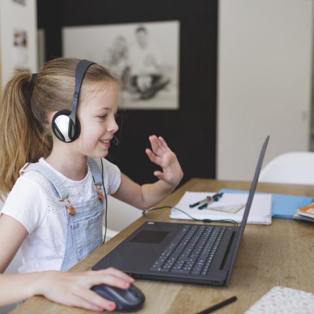 A young girl sitting at a laptop, learning online.