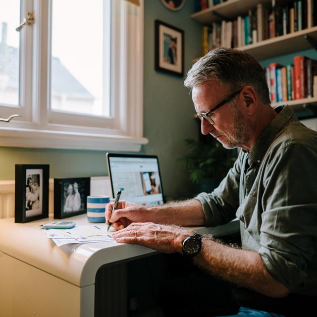 Man sitting at a desk, at home, writing.