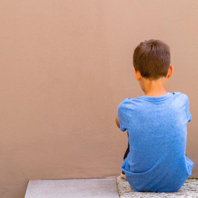 Boy sitting alone in front of a wall