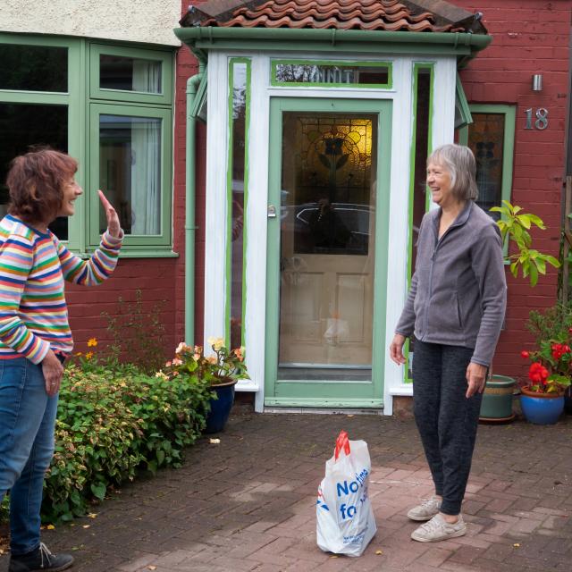 Two neighbours meet outside and socially distanced.