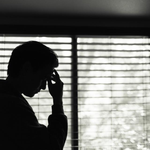 Man in a dark room looking worried, putting his hand to his temple