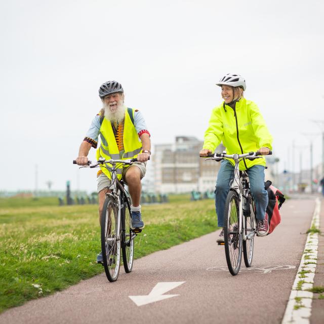 Man and woman cycling in a cycle lane, wearing high-vis, smiling.