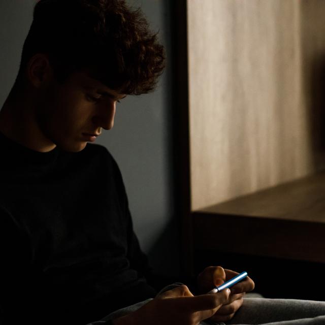 Young man using his phone in a dark room