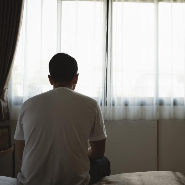 Man sitting alone in a room on a bed. His face is not showing.