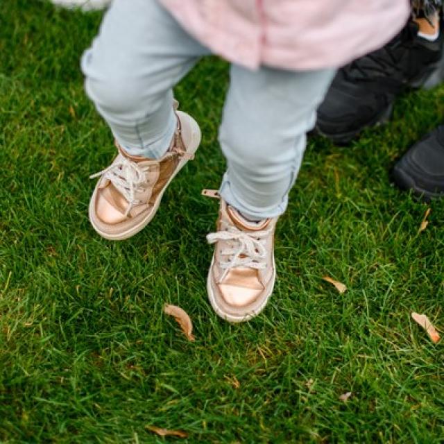 Image showing a family from above so only their legs and feet are visible. Parents and one child, standing on grass.