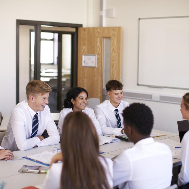 secondary school students sitting around a desk in a classroom.