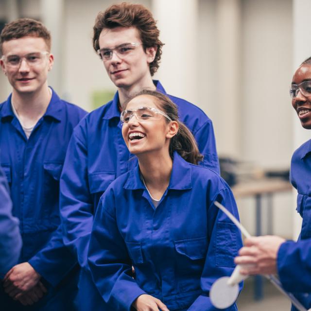 Group of student apprentices wearing blue overalls laughing and smiling in class.