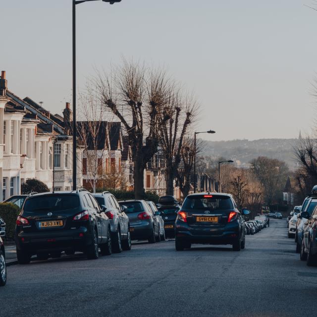 Car drives past cars parked on both sides of a street in Palmers Green, a suburban area of the London Borough of Enfield in North London, England.