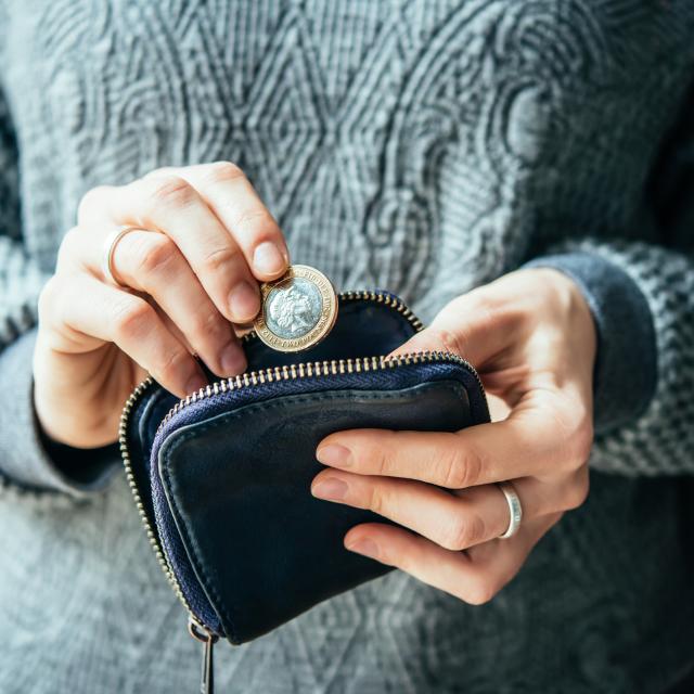 Hands holding british pound coin and small money pouch