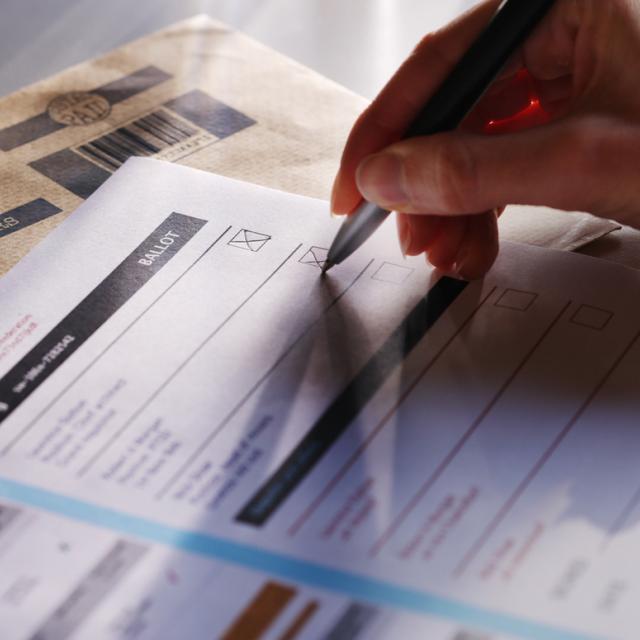 Stock image showing a person's hand filling in a postal ballot / voting form.