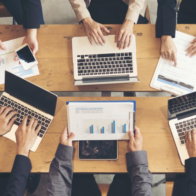 People working collaboratively with multiple laptops on desk