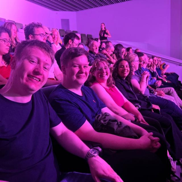 Group of people in an auditorium or theatre, smiling.