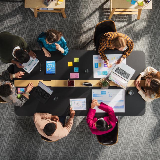 Workplace photo from above - people sitting around the meeting table discussing.