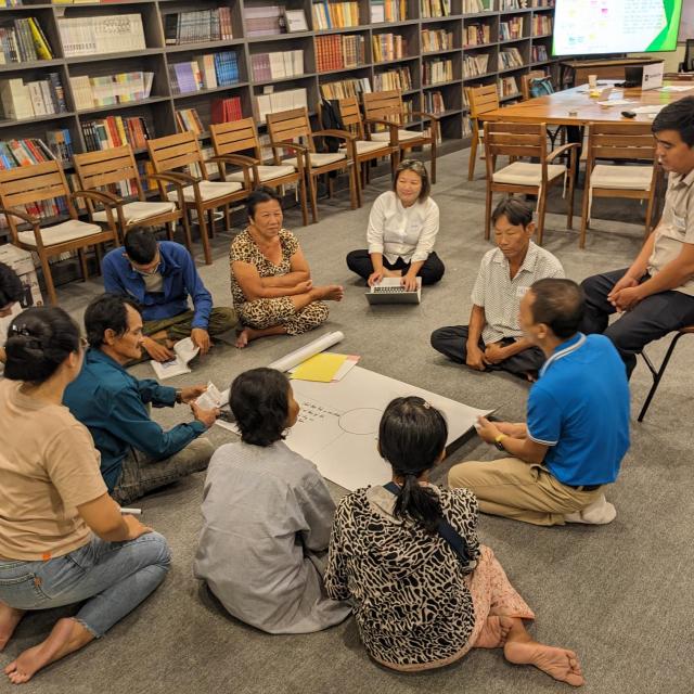 Group of people sitting in a circle on the floor, evidently in engaged discussion and participation