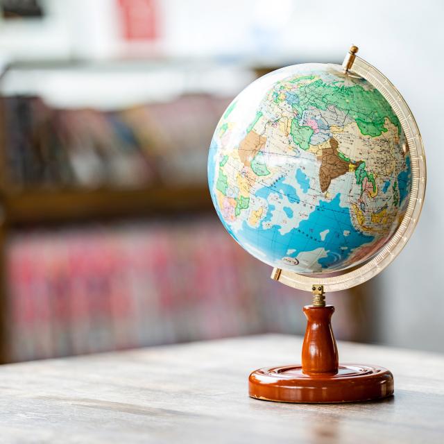 A globe on a desk in the foreground, blurred bookshelves in the background