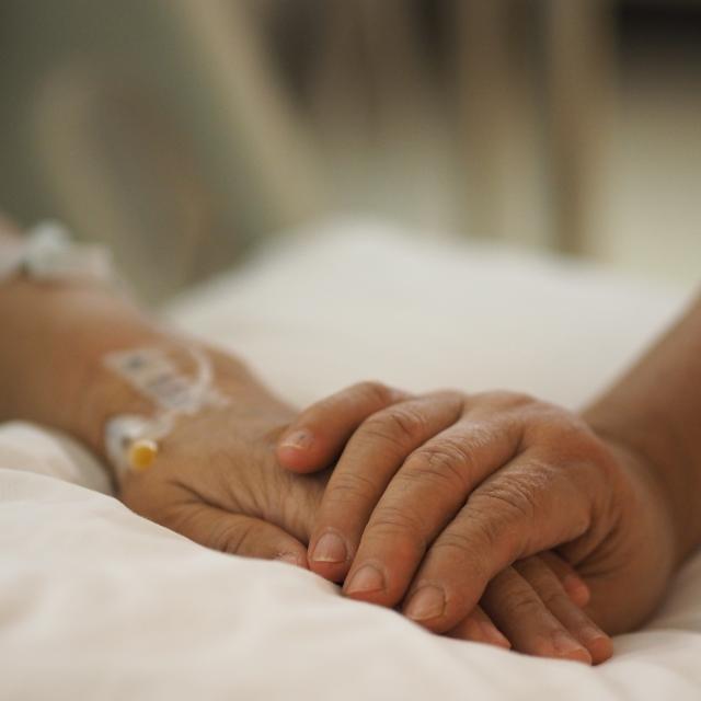 Close up hands comforting patient in hospital bed.