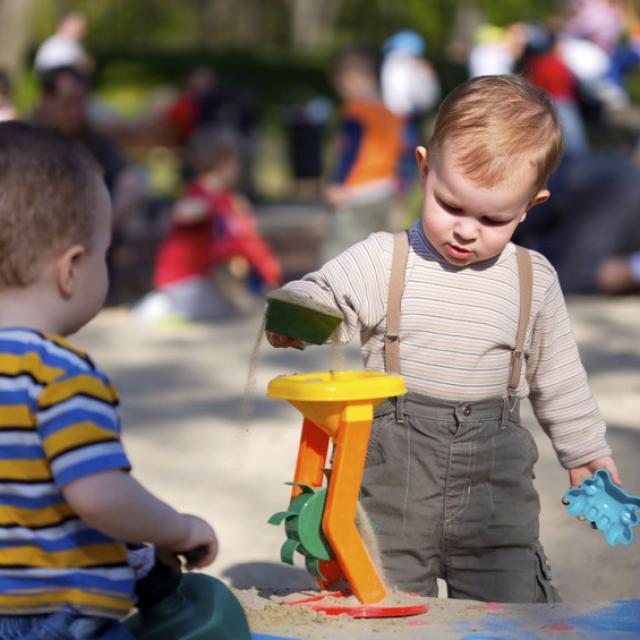 Two boys playing in a sand pit in a playground 
