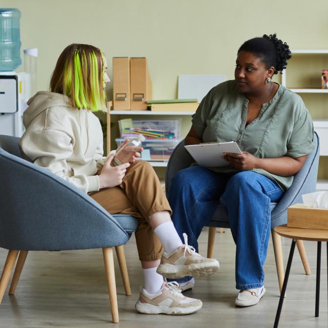 Two people sitting, talking - one young teen talking to older teacher or support worker.