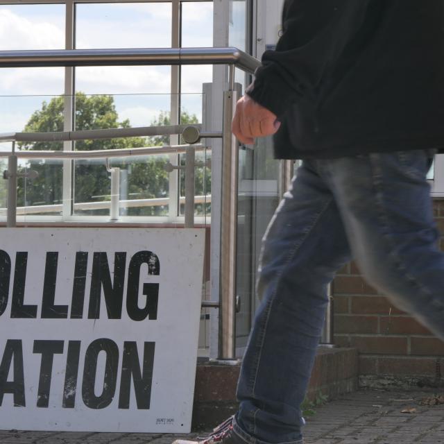 Polling station sign on the ground as someone unidentifiable walks by. 