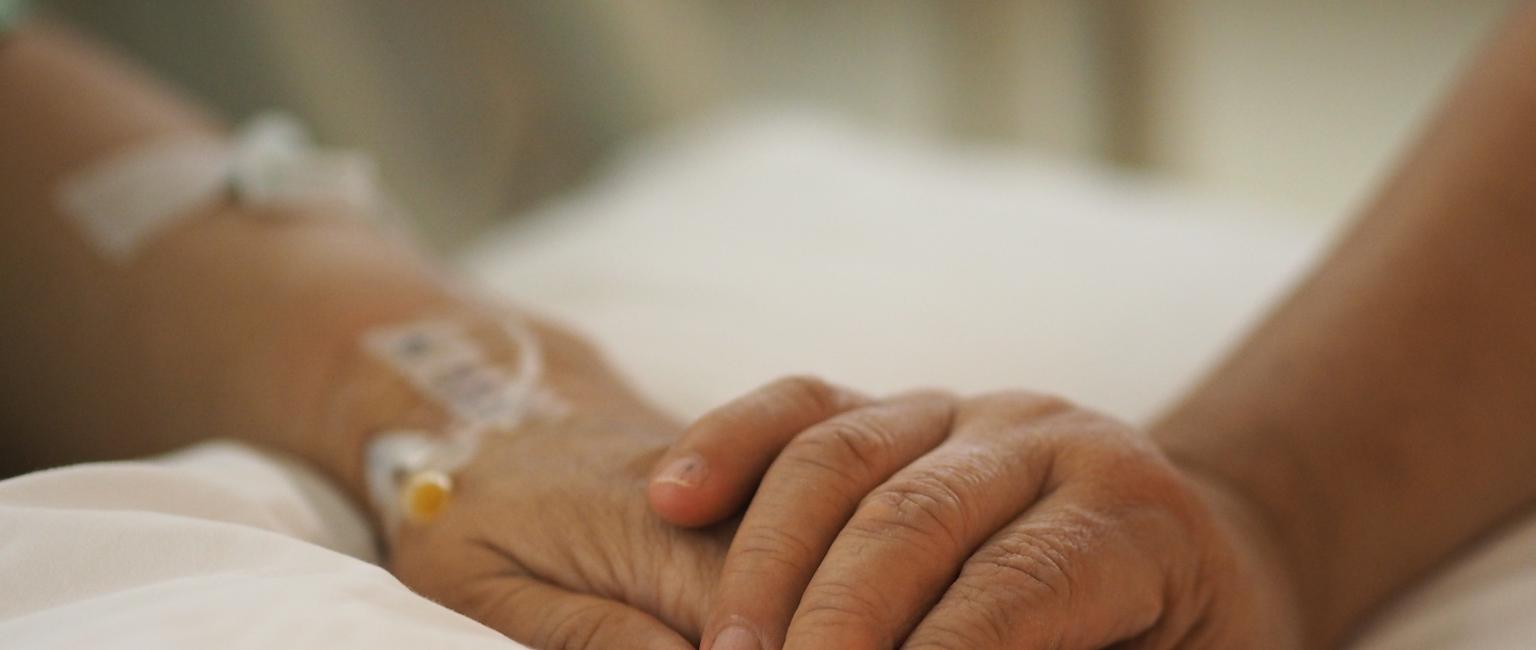Close up hands comforting patient in hospital bed.