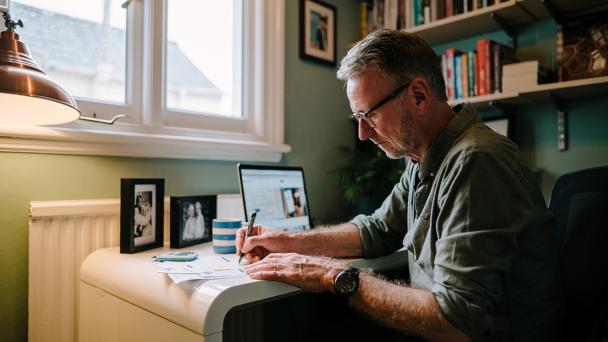 Man sitting at a desk, at home, writing.
