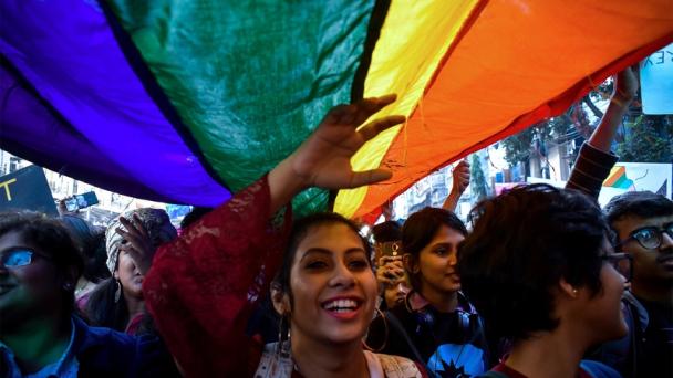 Image of a woman underneath a LGBTQ+ flag at a pride walk