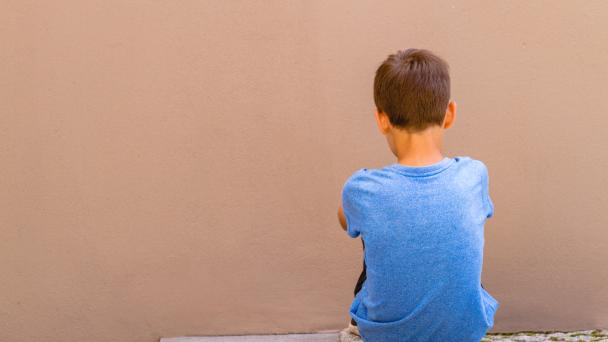 Boy sitting alone in front of a wall