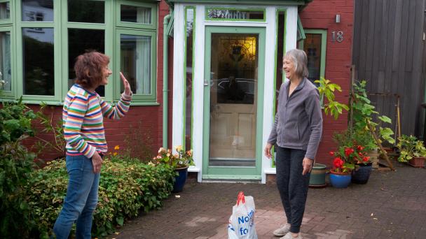 Two neighbours meet outside and socially distanced.