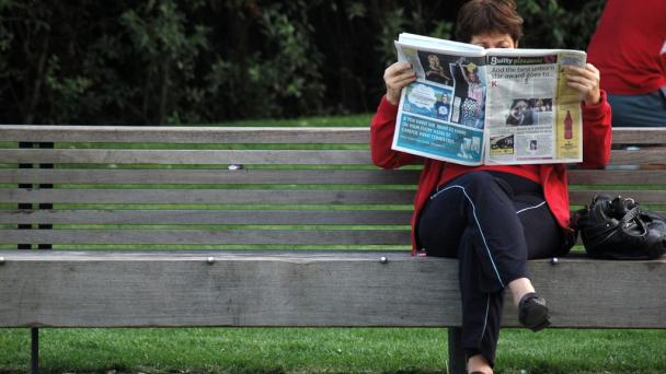 Woman sitting on a bench, reading a newspaper.