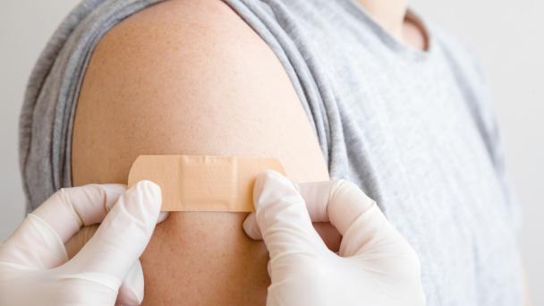 A nurse or doctor applying a plaster to another patients arm after a vaccine.