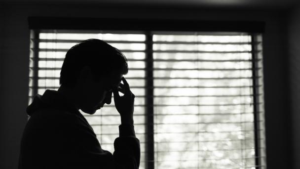 Man in a dark room looking worried, putting his hand to his temple