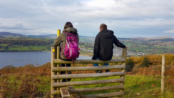Two people sitting on gate looking over estuary in Wales