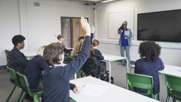 Student raises his hand in class, participating in discussion and one child sitting using a wheelchair