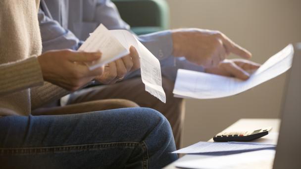 Two people who's heads are not showing, sitting down and looking over receipts or bills. 