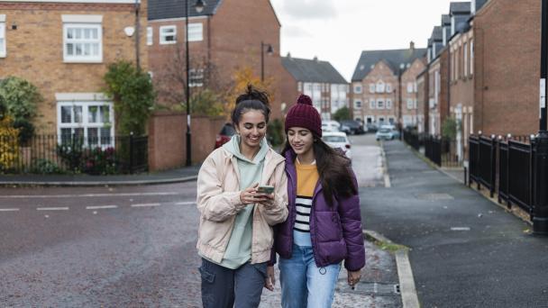 Two girls, Generation Z, walking and laughing while looking at a phone. 