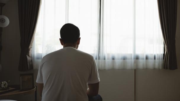 Man sitting alone in a room on a bed. His face is not showing.