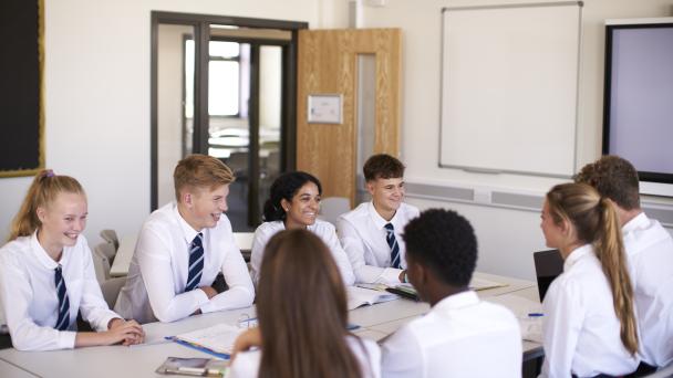 secondary school students sitting around a desk in a classroom.