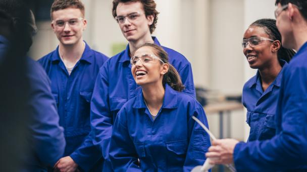 Group of student apprentices wearing blue overalls laughing and smiling in class.