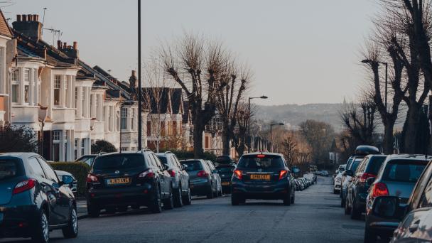 Car drives past cars parked on both sides of a street in Palmers Green, a suburban area of the London Borough of Enfield in North London, England.