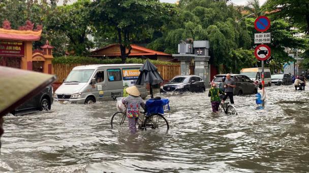 A woman crosses a flooded street with her bicycle in Vietnam