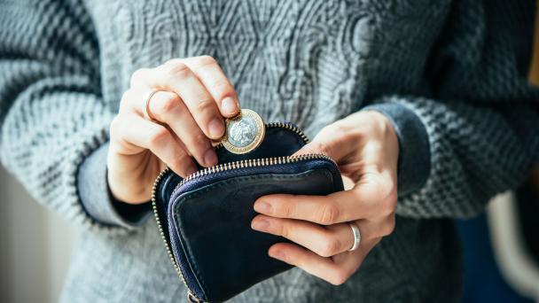 Hands holding british pound coin and small money pouch