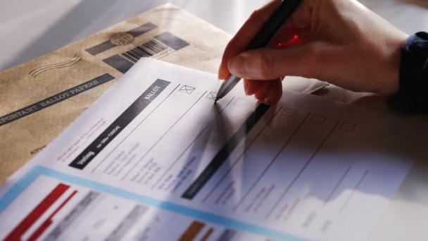 Stock image showing a person's hand filling in a postal ballot / voting form.