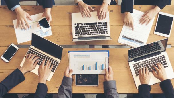 People working collaboratively with multiple laptops on desk