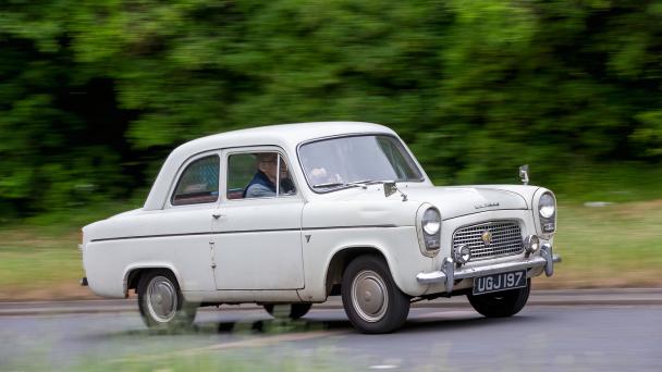 Ford Anglia classic car driving on a British road.