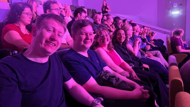 Group of people in an auditorium or theatre, smiling.