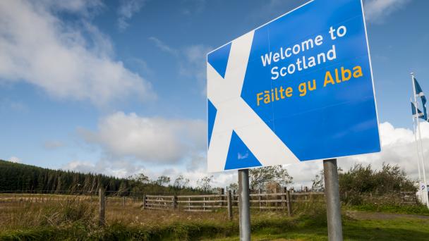 "Welcome to Scotland" sign showing saltire flag emblem at roadside on Scotland/England border. Gaelic translation "Failte gu Abla" shown underneath in yellow text.