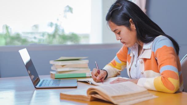 Young person studying from home with laptop and books