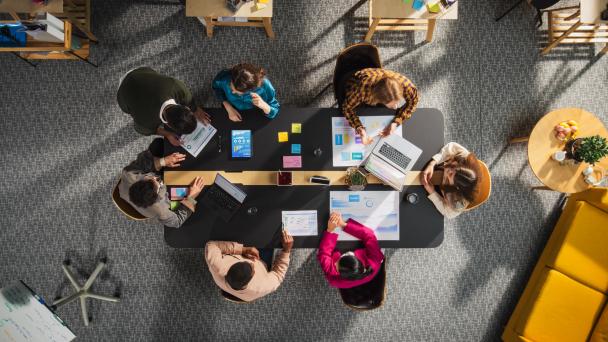 Workplace photo from above - people sitting around the meeting table discussing.
