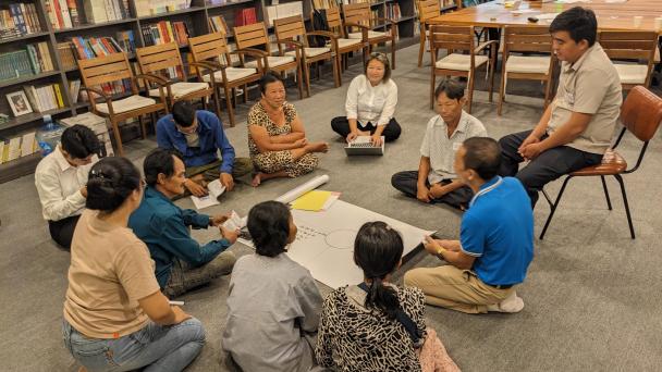 Group of people sitting in a circle on the floor, evidently in engaged discussion and participation