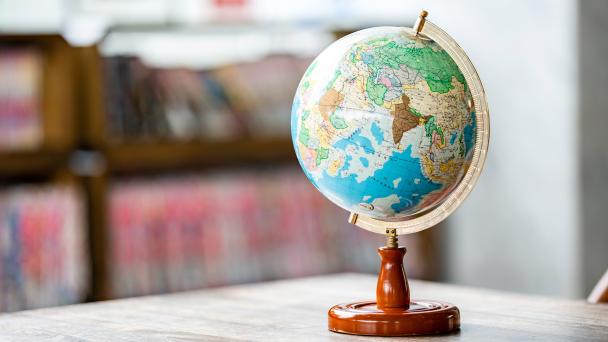 A globe on a desk in the foreground, blurred bookshelves in the background